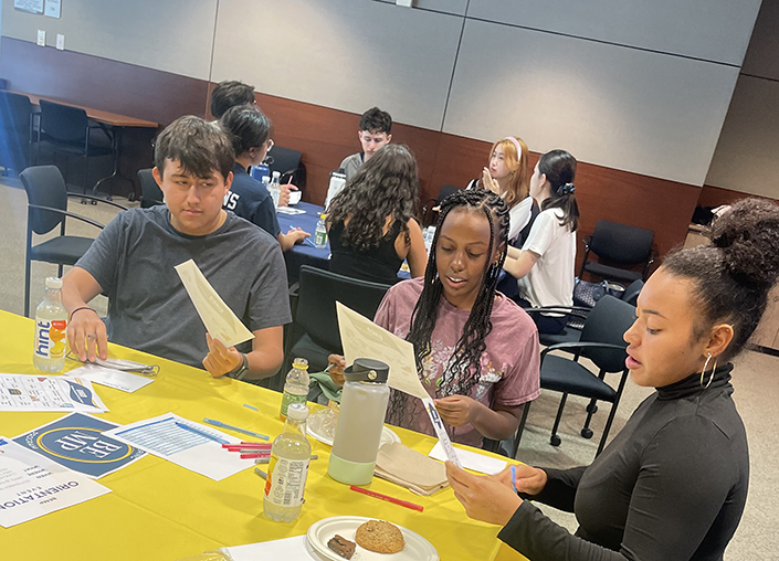 Group of students looking at flyers and brochures at yellow table.