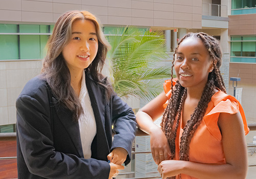 Close-up portrait of Grace Njuguna and Andrea Lai talking at a conference table.