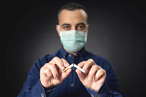 Man breaking a cigarette in half while wearing a face mask